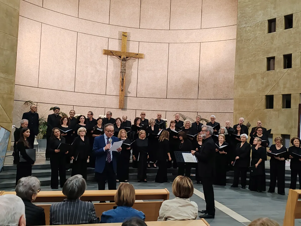 Il Coro Imago Vocis 26 schierato sul presbiterio della Parrocchia Spirito Santo, sotto il crocifisso, mentre un presentatore parla al microfono